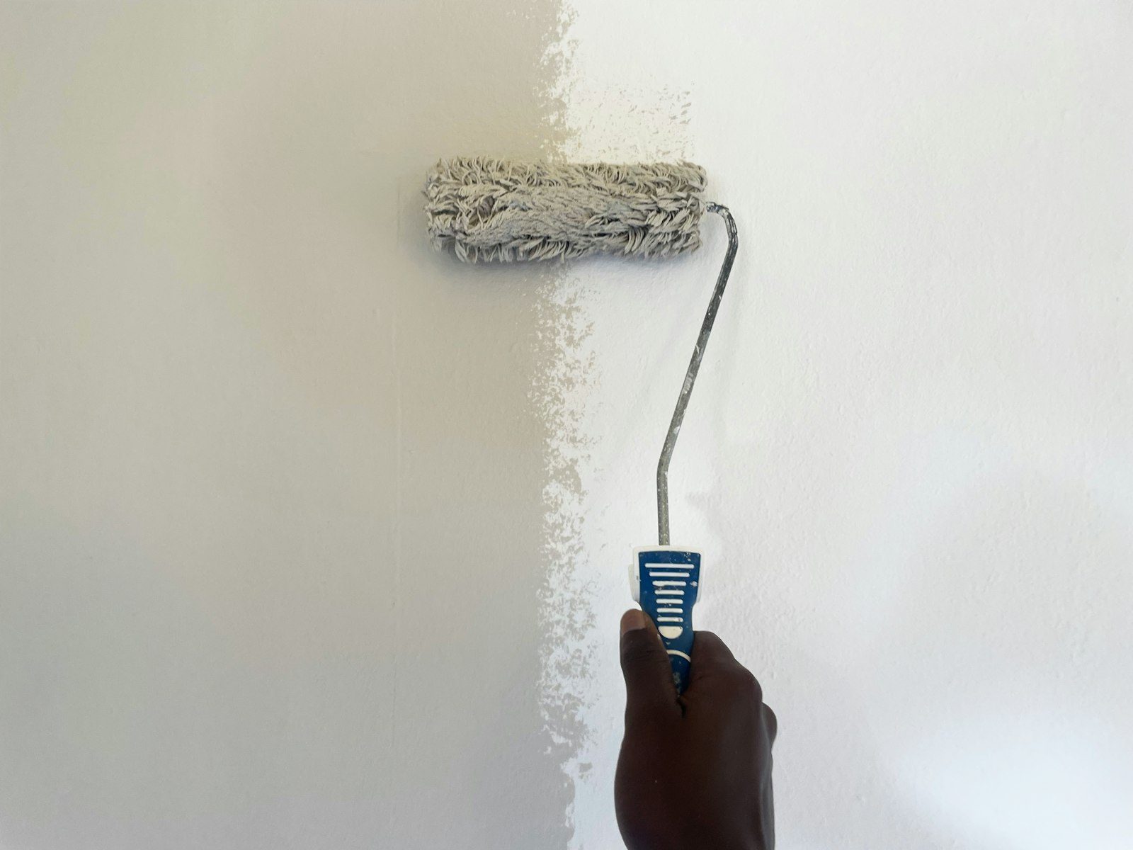 Moderne Website für einen Malerbetrieb, Beispielansicht: Hand mit Farbrolle streicht eine Wand weiß, links ist die Fläche schon deckend gestrichen